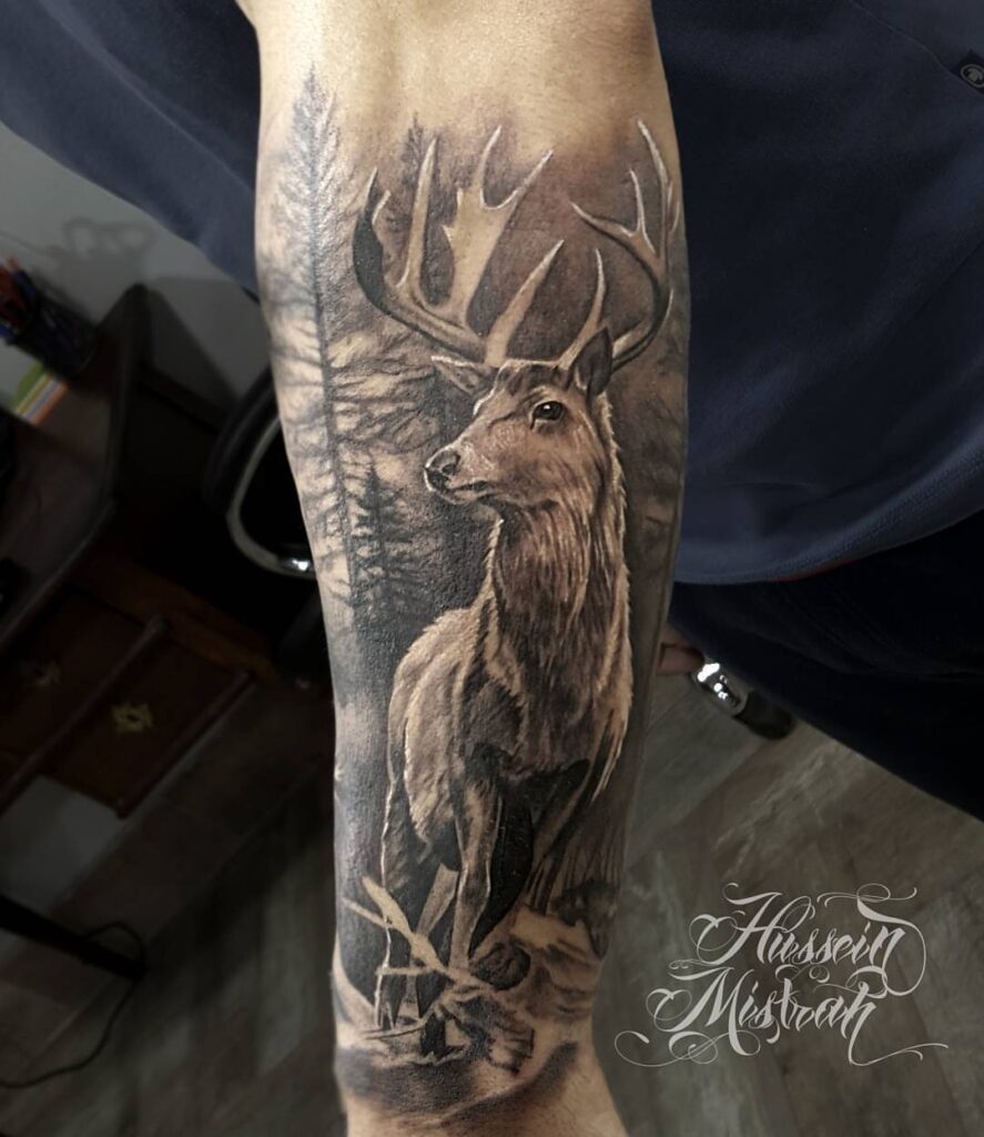 Auf dem Unterarm ist ein Hirsch abgebildet. Das Tattoo ist detailliert und naturalistisch, hinter dem Hirsch ist ein Wald gezeichnet.