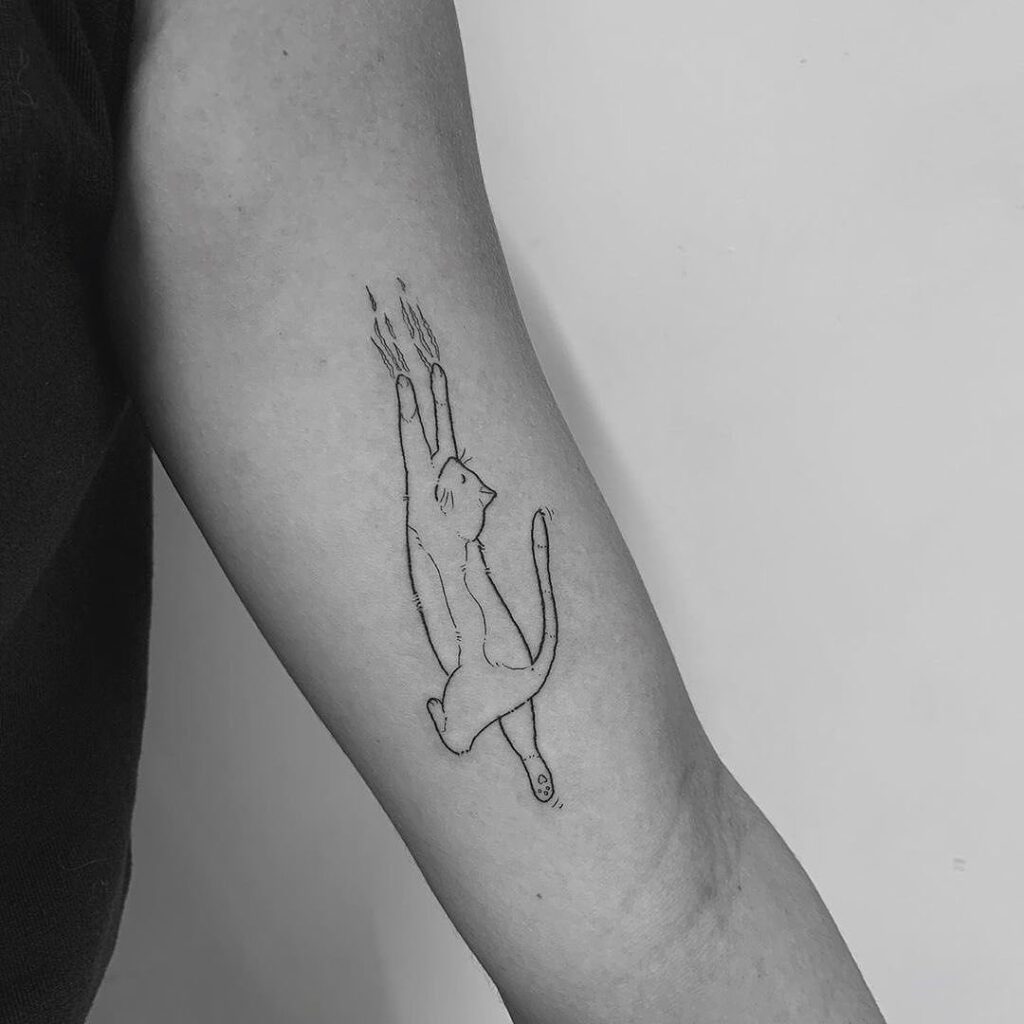 Bild in schwarz-weiss, ein minimalistisches Tattoo einer Katze ist auf einem Oberarm zu sehen.