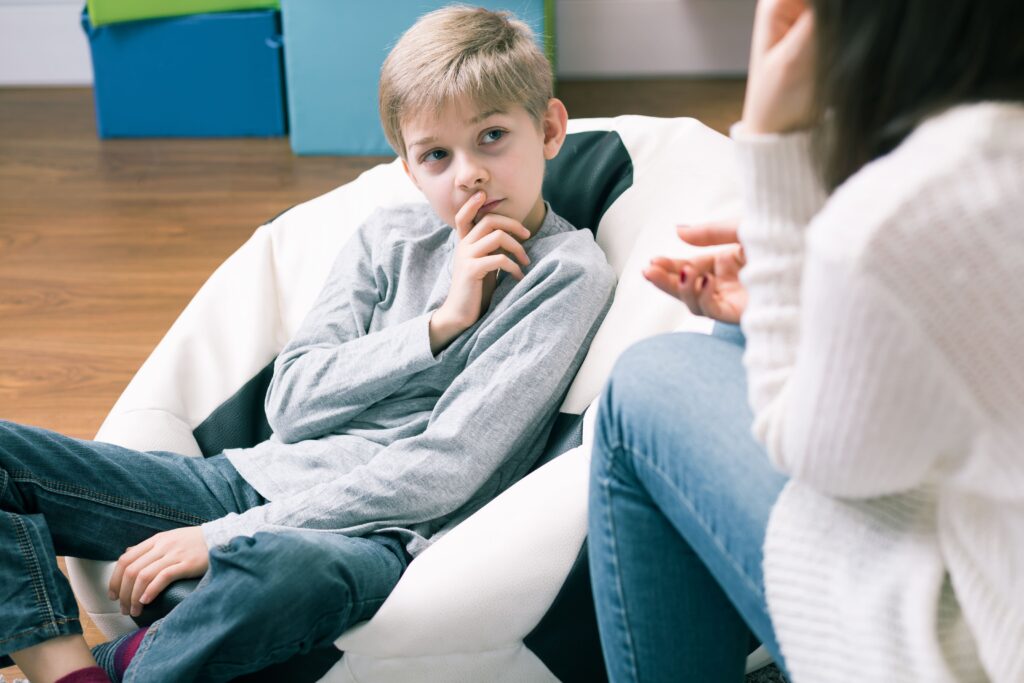 Ein blonder Junge hört einem Psychotherapeuten zu.
