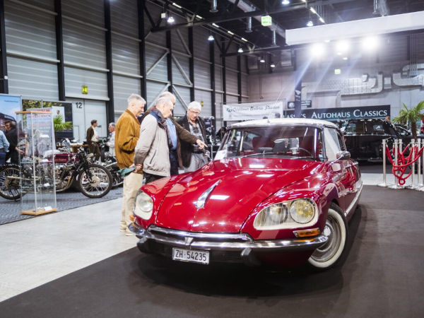 Vier ältere Herren schauen sich ein rotes französisches Auto an.