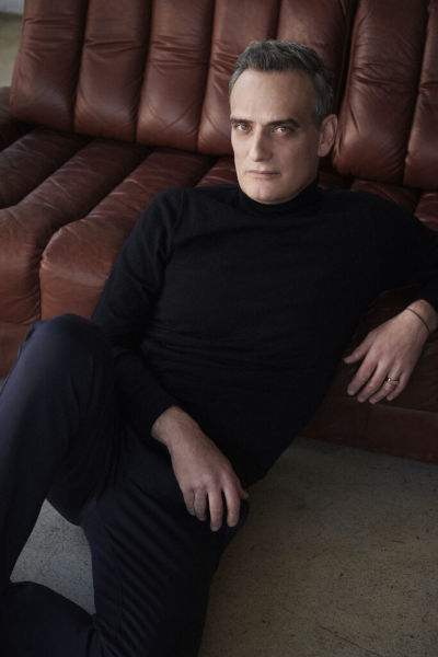 Anatole Taubman sitzt vor einem Sofa