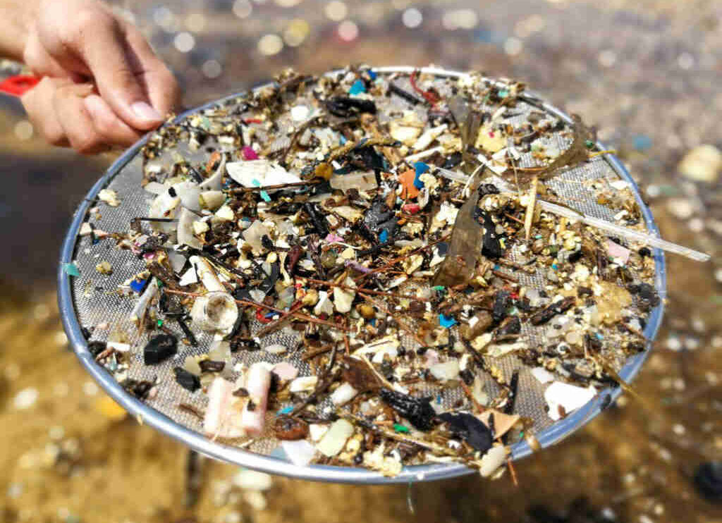 Mit einem Sieb lassen sich grosse Plastikstucke vom Sand entfernen.