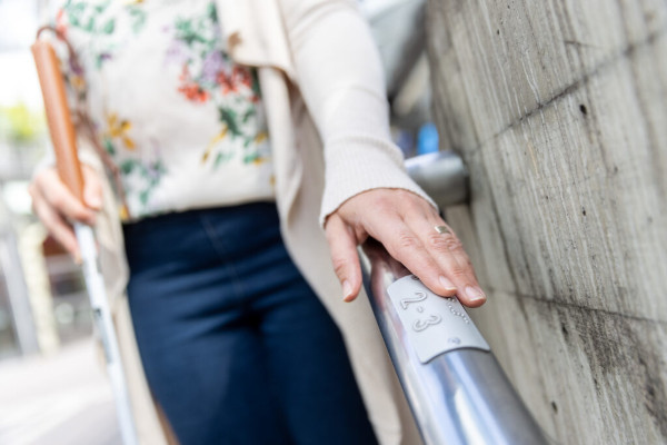 Junge Frau greift nach Geländer mit Brailleschrift am Bahnhof.