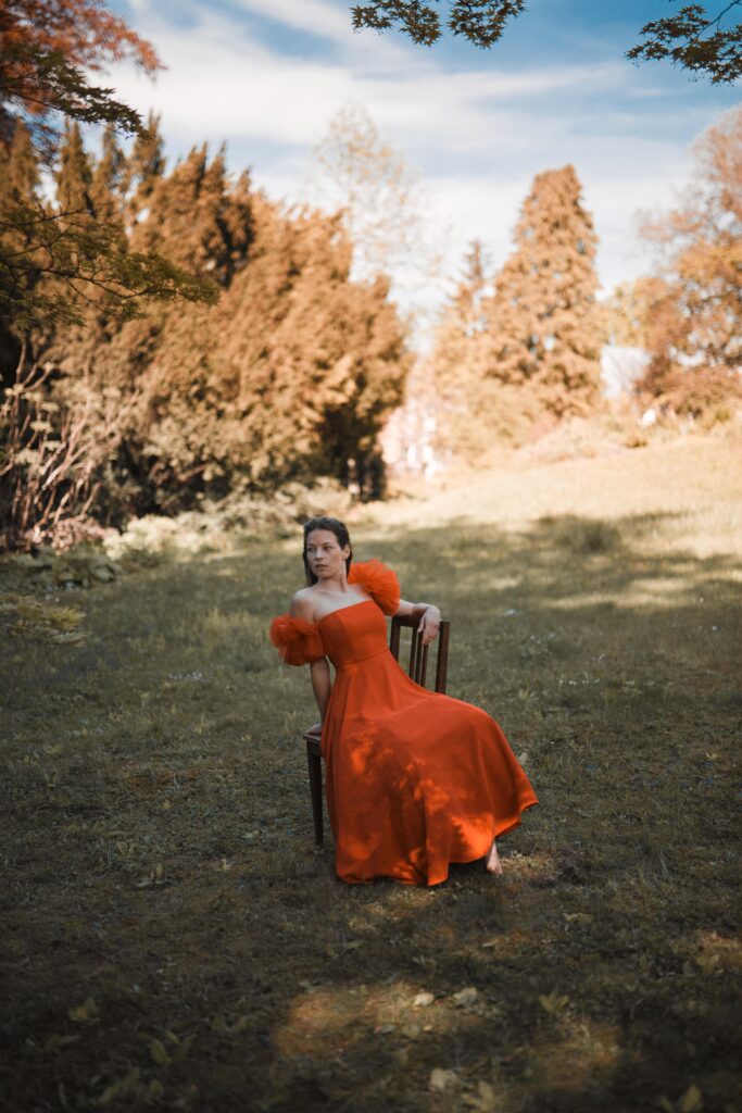 Anna Rossinelli trägt ein rotes Kleid und sitzt auf einem Stuhl auf einer Wiese