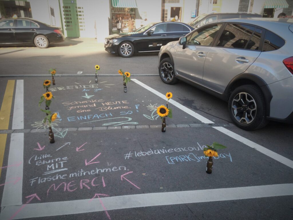 Auf einem Parkplatz stehen Sonnenblumen in Glasflaschen gratis zum Mitnehmen.