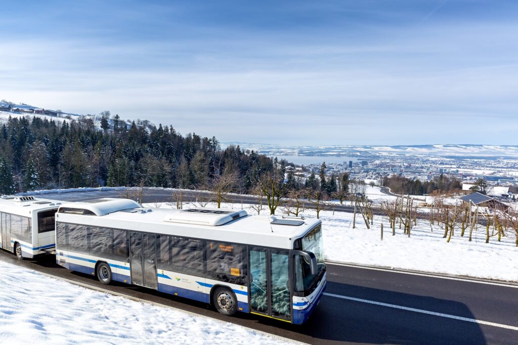 Ein Bus fährt auf einem Hügel, im Hintergrund ist die Stadt Zug zu sehen.