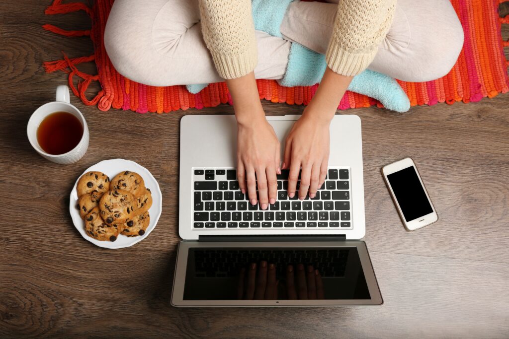 Eine Frau sitzt vor dem Laptop, daneben steht ein Teller mit Keksen.