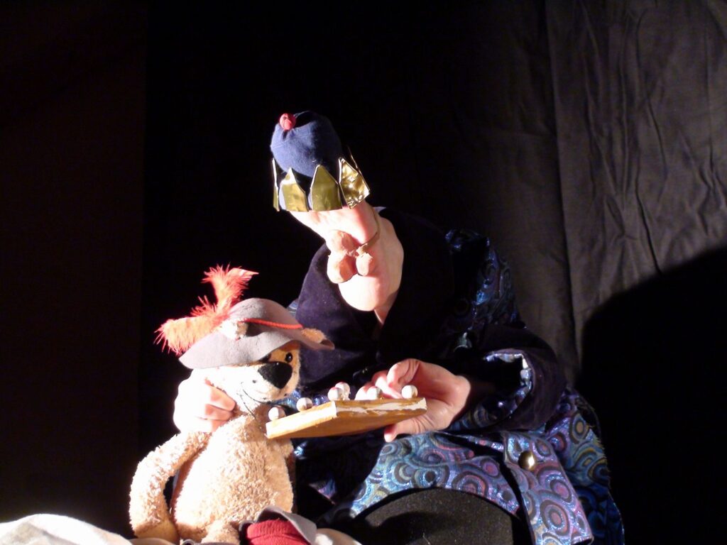 Ein in ein Gewand gekleideter Fuss bietet mit der Hand von Anne Klinge einem Teddybären Pralinen an. Auf der Bühne erwachen die Füsse der Regisseurin zum eigenen Leben.