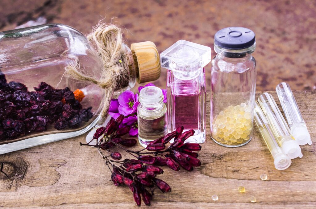 Fläschchen mit veganen Ölen und Blüten liegen auf einem Holztisch.