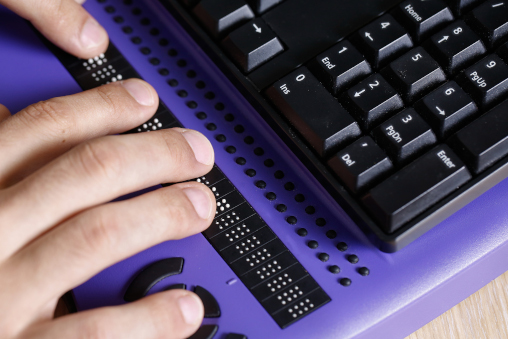 Blind person using computer with braille computer display and a computer keyboard. Blindness aid, visual impairment, independent life concept.