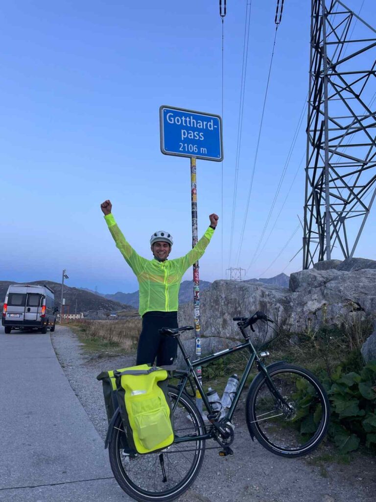 Bolliger steht beim Gotthardpass neben seinem Velo, hebt die Arme hoch.