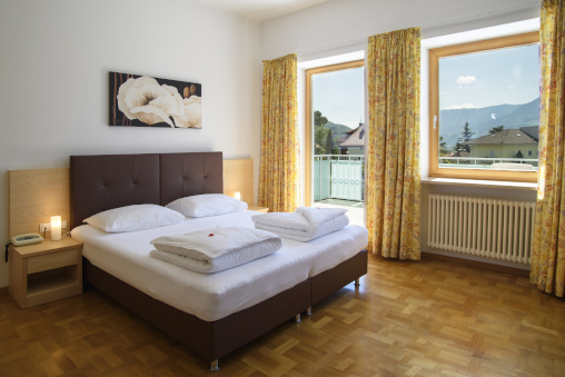 Doppelzimmer im Hotel Filipinum mit Doppelbett, Nachttisch, einem Bild von weissen Blumen über dem Bett und Sicht auf den Balkon.