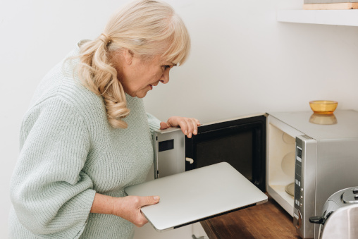 Demenz, alte Frau packt Laptop in Mikrowelle