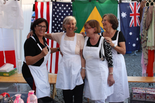 Vier ältere Frauen mit Kochschürzen vor verschiedenen Nationalflaggen.