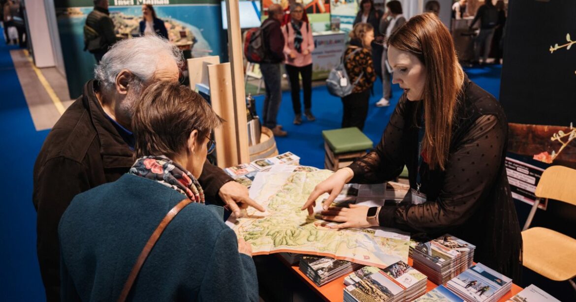 Eine Frau auf der FESPO zeigt Besuchern etwas auf einer Karte.