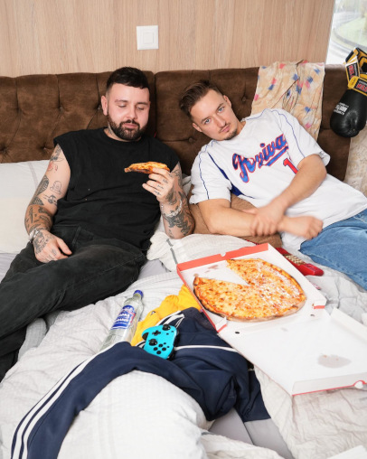 Beide Rapper mit Pizza und Controller im Hotelbett