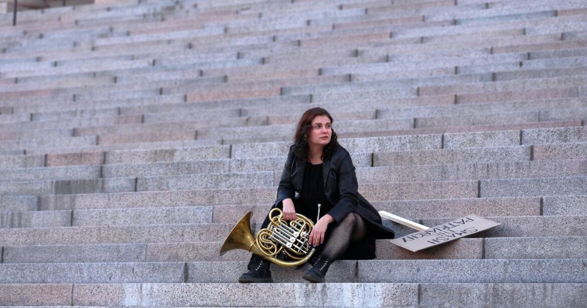 Julia Leskinen sitzt mit Horn in der Hand auf der Treppe. Neben ihr liegt ein Schild, auf dem "Smash the patriarchy" in Grossbuchstaben steht.