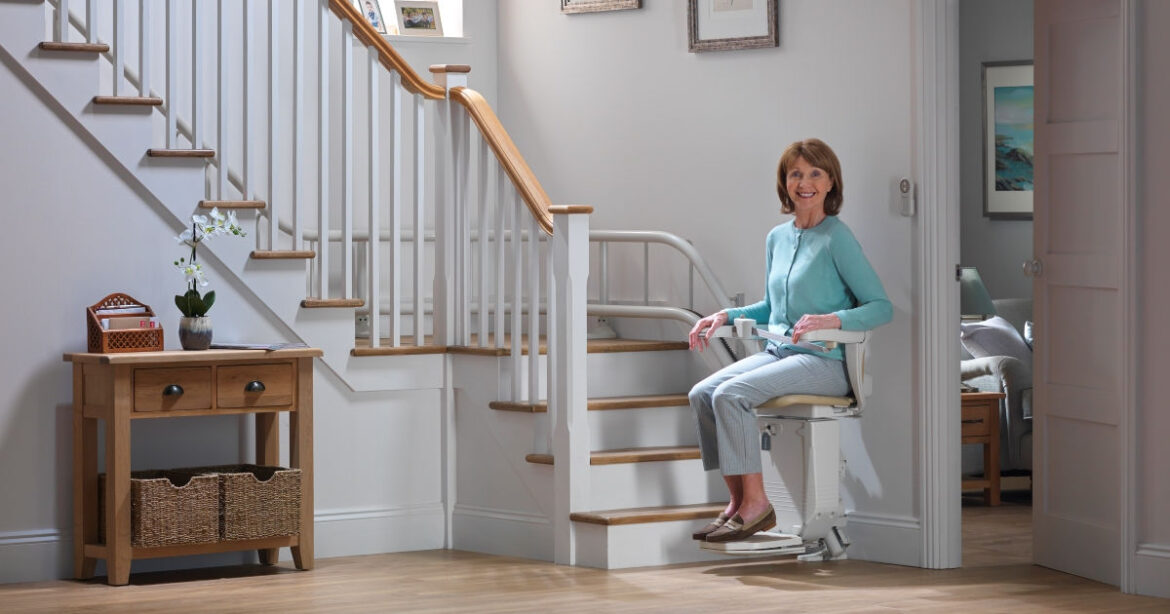 eine Frau sitzt auf einem Treppenlift am Fusse der Treppe in einem Haus
