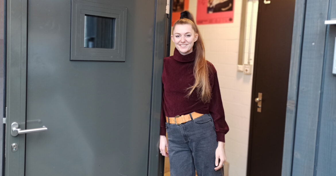 Dana steht neben Tür im Flur