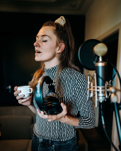 Dana im Studio mit Kaffee und Kopfhörern in den Händen