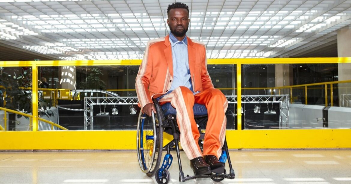 Ein dunkelhäutiger Mann sitzt in einem orangen Sportanzug im Rollstuhl.