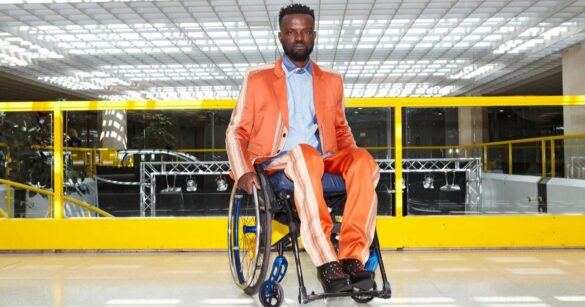 Ein dunkelhäutiger Mann sitzt in einem orangen Sportanzug im Rollstuhl.