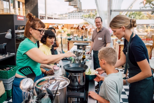 Frauen und ein Kind stehen rund um einen Kochtopf an der Food Zurich