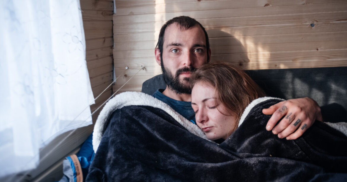 Mann hält Frau in den Armen unter Bettdecke