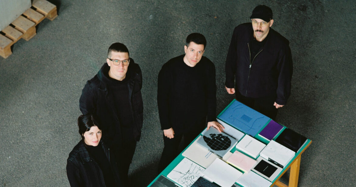 Vier Menschen in schwarz stehen um einen Tisch voller Bücher