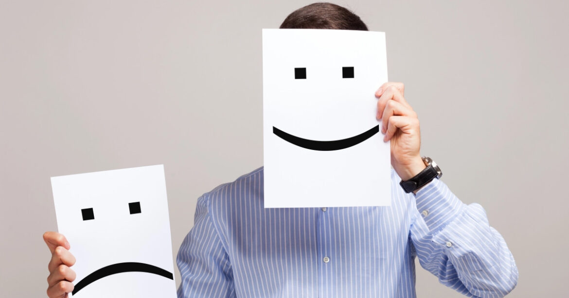 Mann hält sich ein Papier mit einem Smiley vors Gesicht