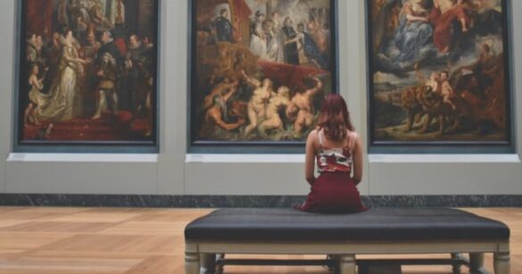 Eine junge Frau sitzt vor drei Gemälden im Museum, wo sie durch MeetByChance.ch auf andere Singles treffen könnte.