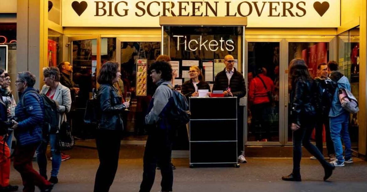 Vor dem Kino stehen Menschen an der Kasse, das Licht fällt sanft auf den Eingang zum Pink Apple Festival.