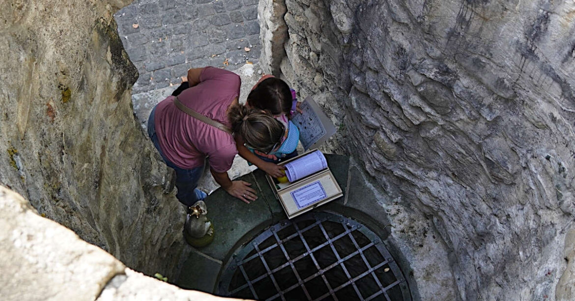 Eine Mutter und ihr Kind stehen beim Brunnen im Museum Burg Zug bei der Schnitzeljagd