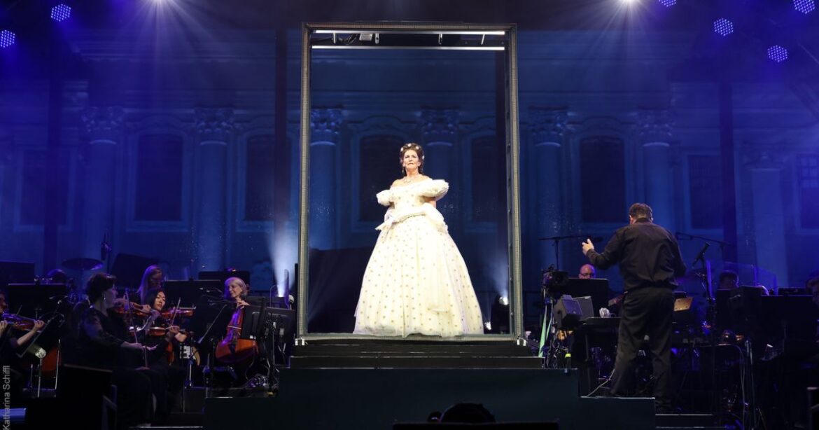 Elisabeth steht in einem weissen Kleid auf der Bühne, umgeben vom Orchester.