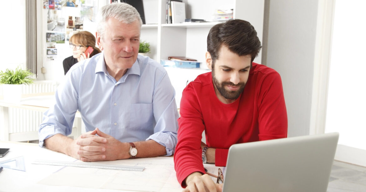 Mann hilft einem älteren Mann bei der Arbeit am Laptop