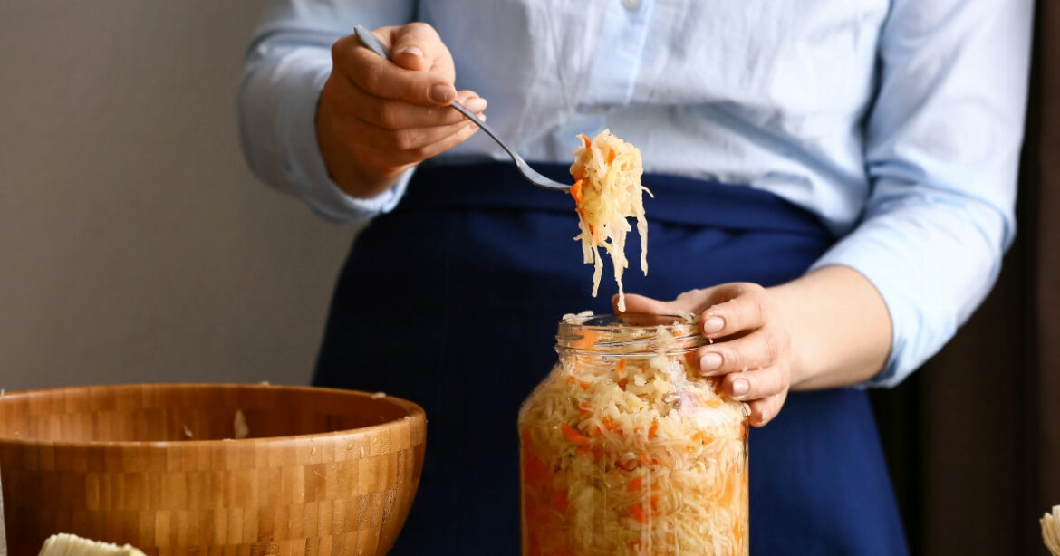 Eine Frau schöpft mit einer Gabel Sauerkraut aus einem grossen Glas