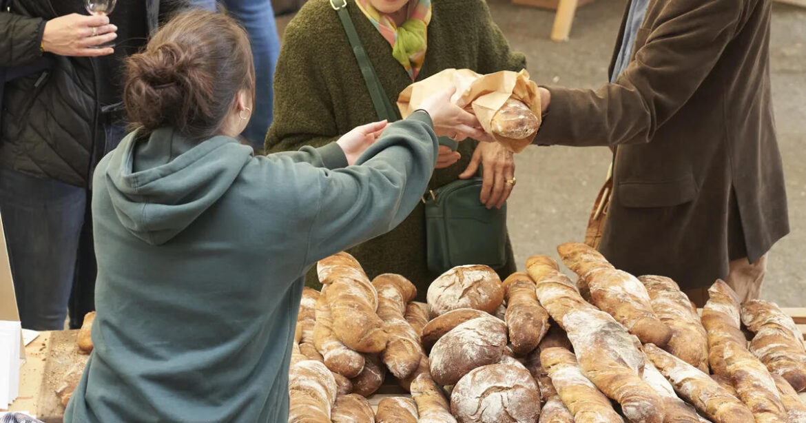 Eine Frau reicht Besuchern Brot in der Mühle Tiefenbrunnen am Markt