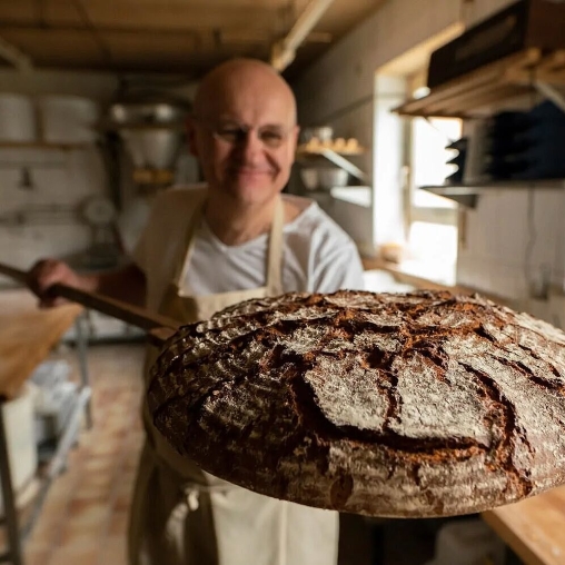 Ein Bäcker zeigt frischgebackenes Brot in die Kamera in der Backstube