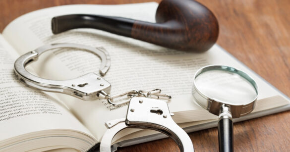 Ein aufgeschlagenes Buch liegt auf dem Tisch, darauf eine Pfeife und Handschellen