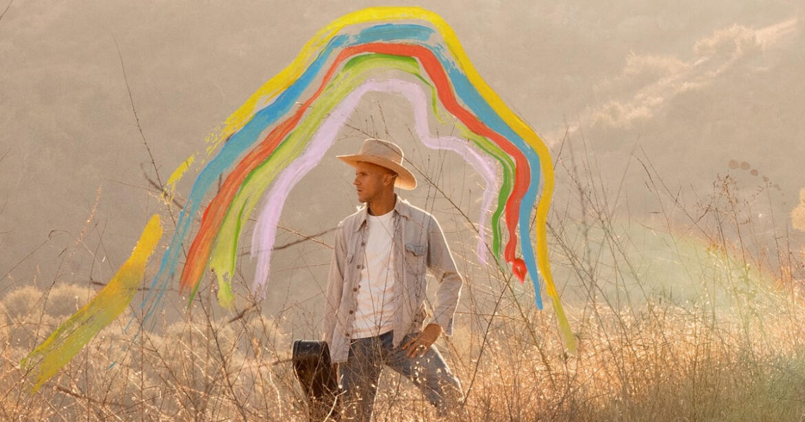 Singer-Songwriter Milow steht in einem Feld mit Instrument in der Hand