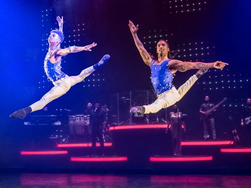 Zwei tanzende Männer springen in die Luft mit Live-Band im Hintergrund auf der Bühne bei Ballet Revolucion